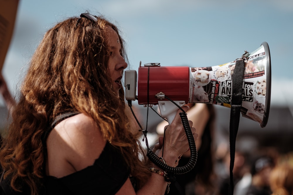 Fotografia de foco seletivo de mulher vestindo camisa preta de ombro frio usando megafone durante o dia