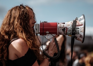 selective focus photography of woman wearing black cold-shoulder shirt using megaphone during daytime