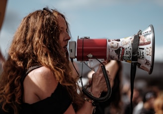 selective focus photography of woman wearing black cold-shoulder shirt using megaphone during daytime