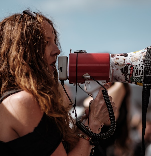 selective focus photography of woman wearing black cold-shoulder shirt using megaphone during daytime