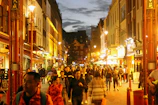 A bustling city street at dusk, lights glowing warmly as people move through the scene.
