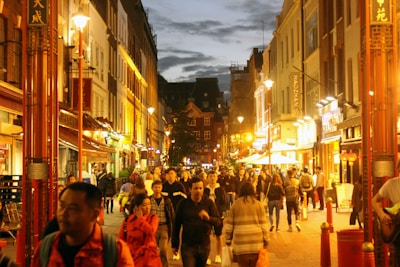 A bustling city street at dusk with colorful lights and lively crowds.