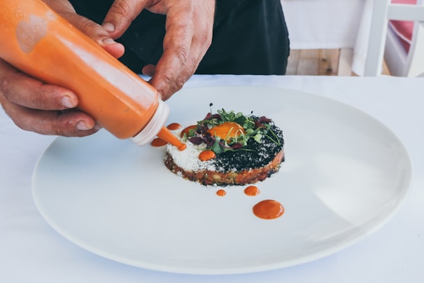 A chef’s hands delicately garnishing a signature entrée with microgreens.