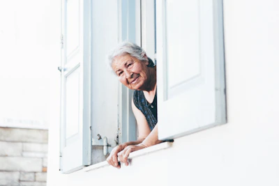 A warm, friendly carer gently supporting an elderly woman at home, smiling together by the window