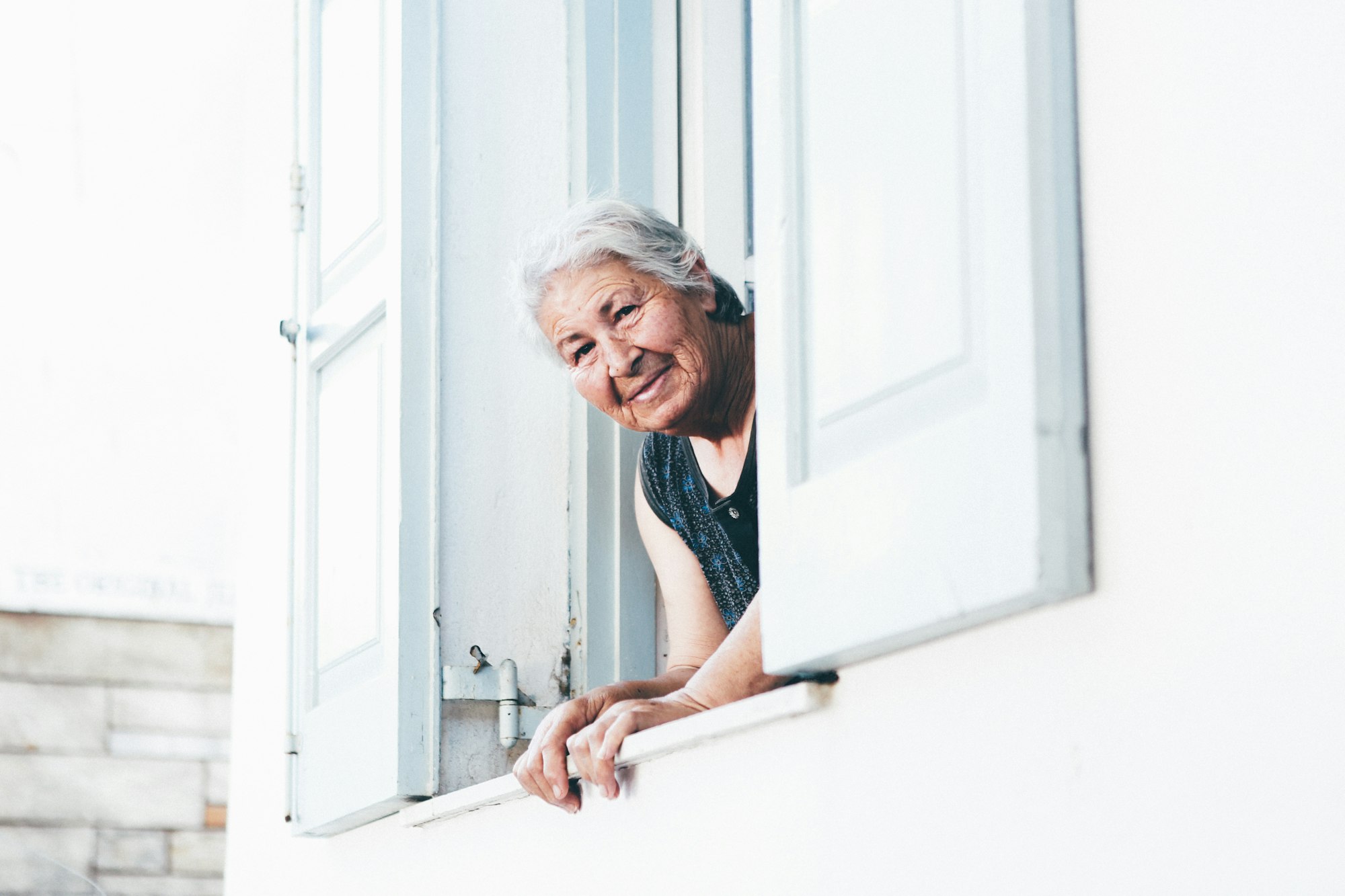 An elderly woman peeking outside a window