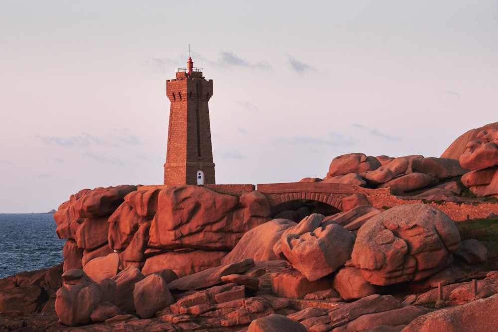 brown lighthouse on rock cliff near body of water