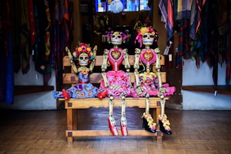 three Frida Kahlo skeleton dolls sitting on bench