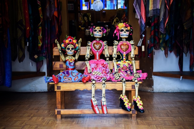 three Frida Kahlo skeleton dolls sitting on bench