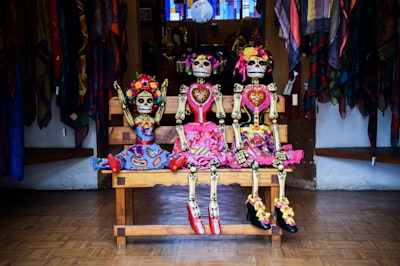 three frida kahlo skeleton dolls sitting on bench day of the dead google meet background