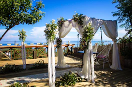 A beautifully decorated wedding arch with flowing fabrics and natural flowers in soft pastel tones.