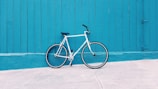 white road bike leaning on teal wooden wall during daytime