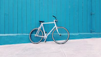 white road bike leaning on teal wooden wall during daytime