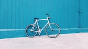 white road bike leaning on teal wooden wall during daytime