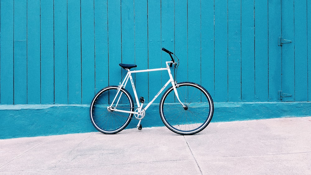 white road bike leaning on teal wooden wall during daytime