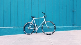 white road bike leaning on teal wooden wall during daytime