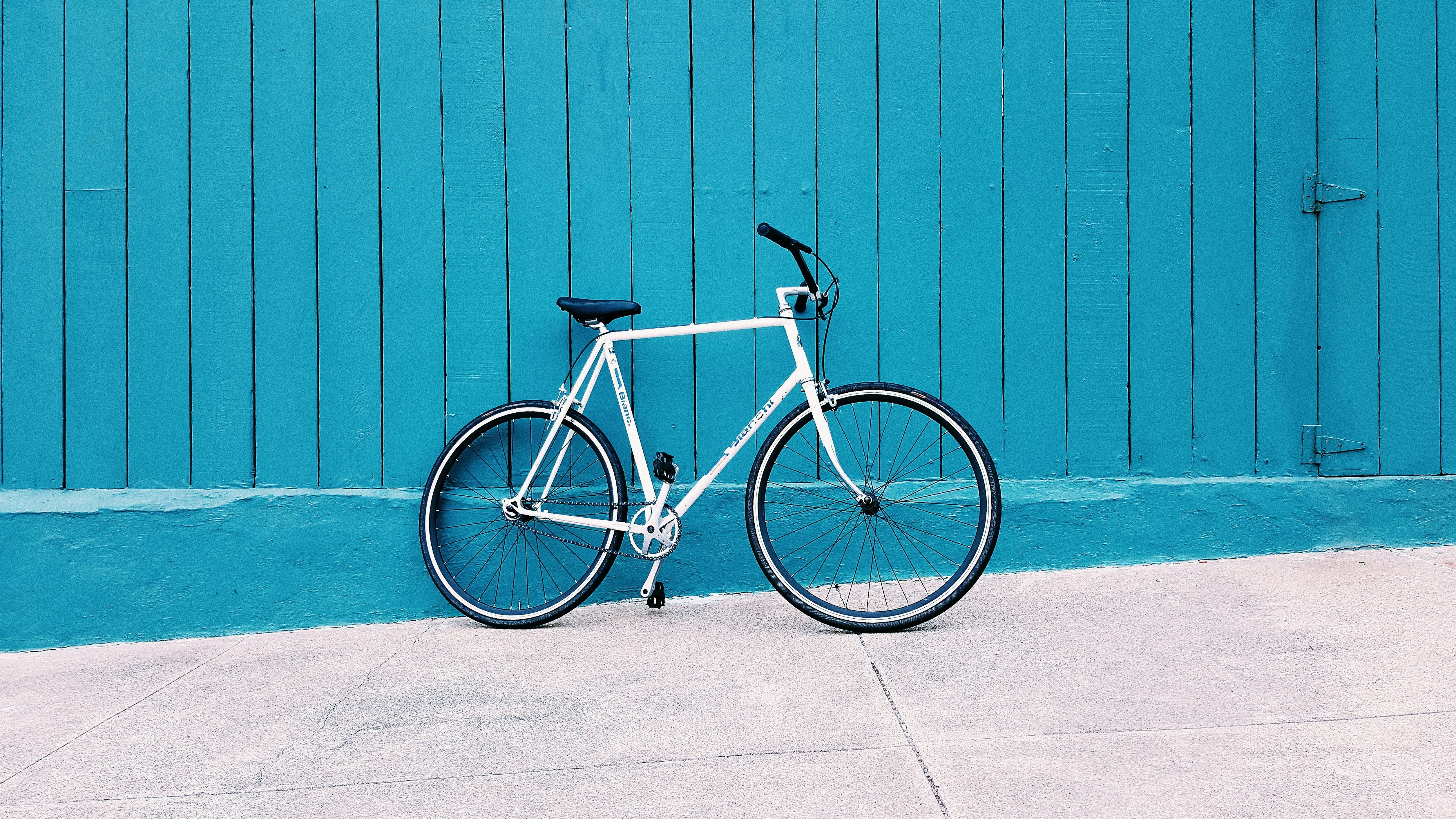 white road bike leaning on teal wooden wall during daytime