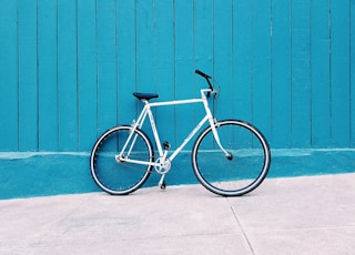 white road bike leaning on teal wooden wall during daytime