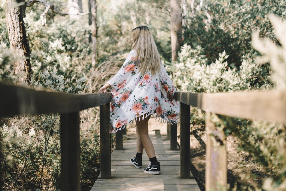 mulher caminhando ao longo da ponte de madeira que leva à floresta