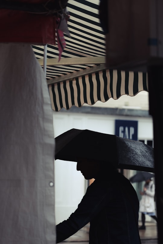 man using umbrella under white and black awning in Cambridge United Kingdom