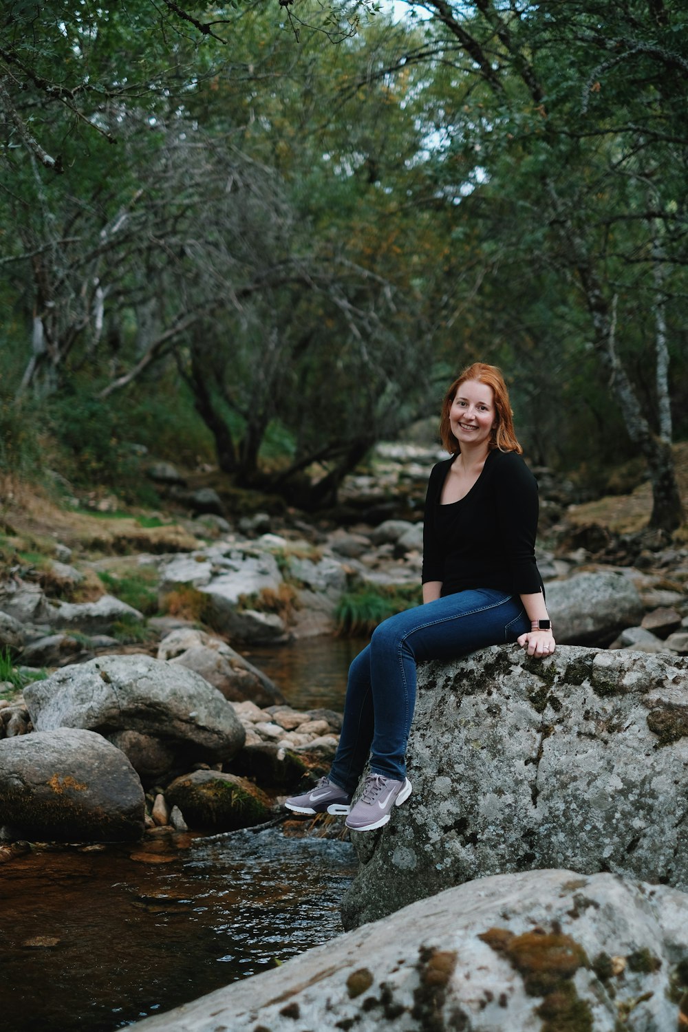 woman sitting on gray rock near body of water at daytime