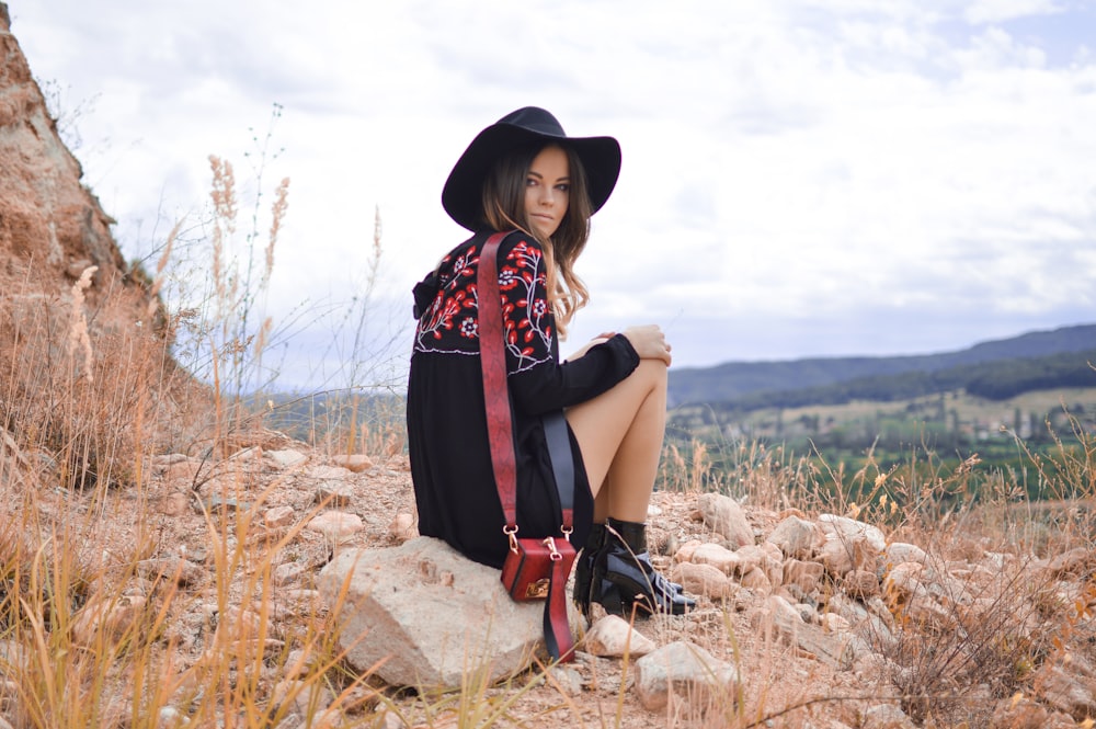 woman sitting on gray boulder near brown grass