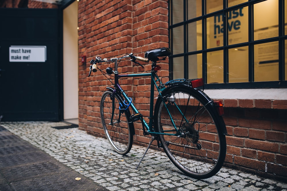 black and blue bicycle parked near a glass window at daytime