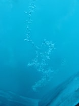 A photograph depicting an underwater scene with light blue tones. The image has bubbles rising through the water, creating an ethereal, almost abstract pattern. The surrounding area is a gradient of different shades of blue, suggesting varying depths and light penetration.