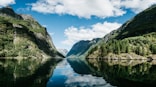 body of water near mountain under white clouds