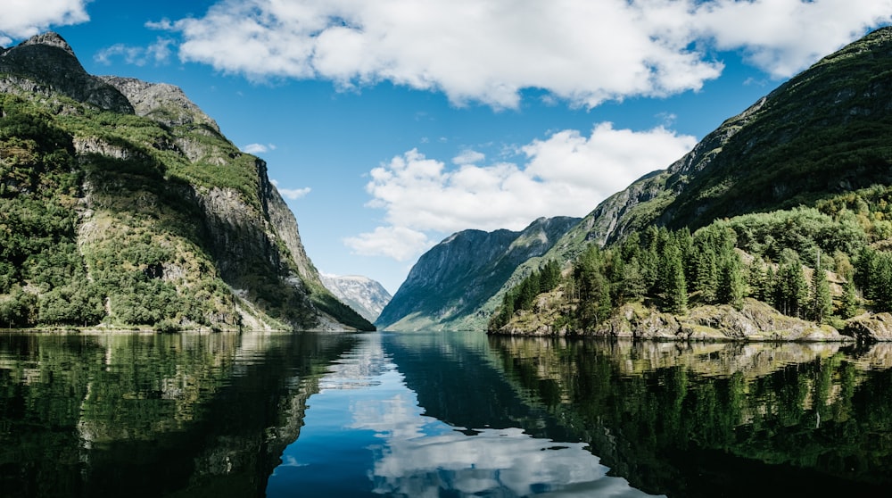 body of water near mountain under white clouds