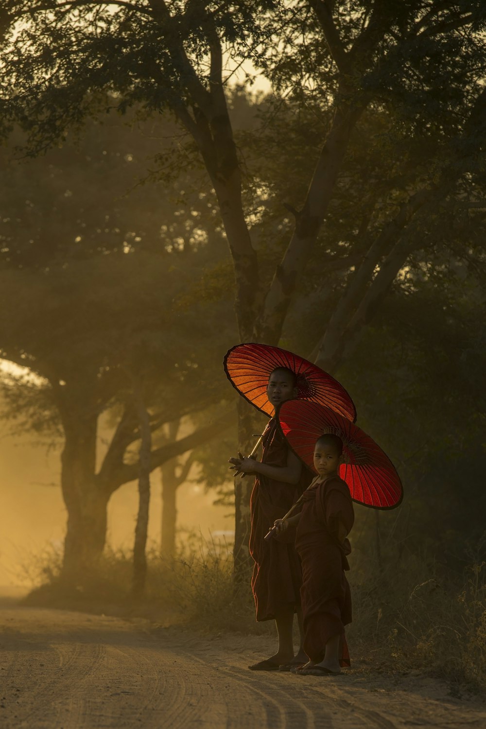 two monks under red wax umbrella surround by green leafed trees