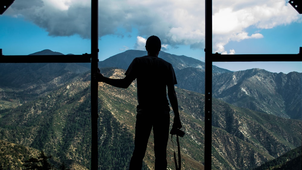silhouette photo of person standing near door overlooking mountain during daytime