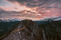 A rugged alpine ridgeline with hikers silhouetted against a vibrant sunset sky.