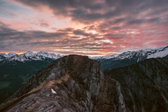 A rugged alpine ridgeline with hikers silhouetted against a vibrant sunset sky.