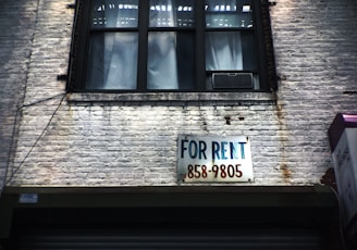 for rent sign on wall below window glass of building