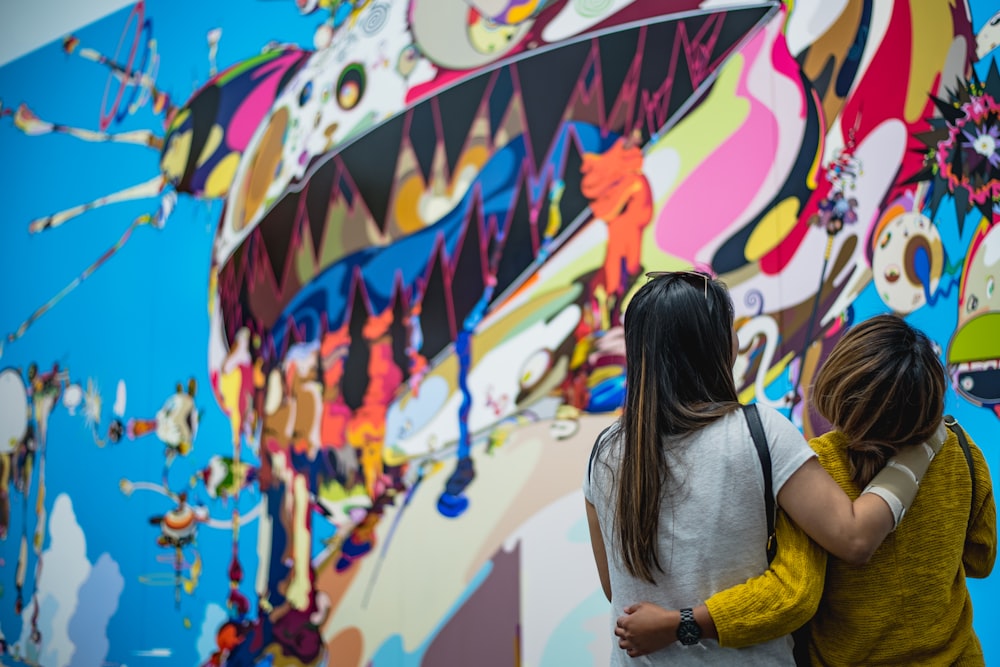 two women looking in front of wall painting