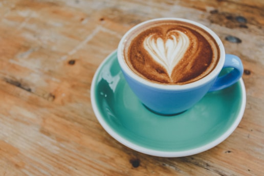 A sunlit latte art heart resting on a rustic wooden table near a window with soft morning light.