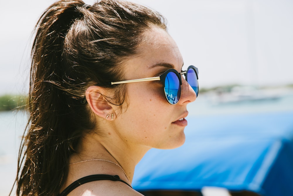 woman in blue sunglasses in front of blue car during daytime shallow focus photography
