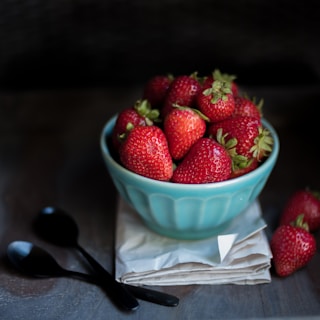 strawberry fruit on blue ceramic bowl beside two black spoons