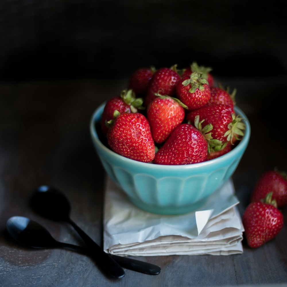 strawberry fruit on blue ceramic bowl beside two black spoons