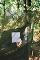 A person relaxing outdoors, reading an ebook on a tablet under a tree.