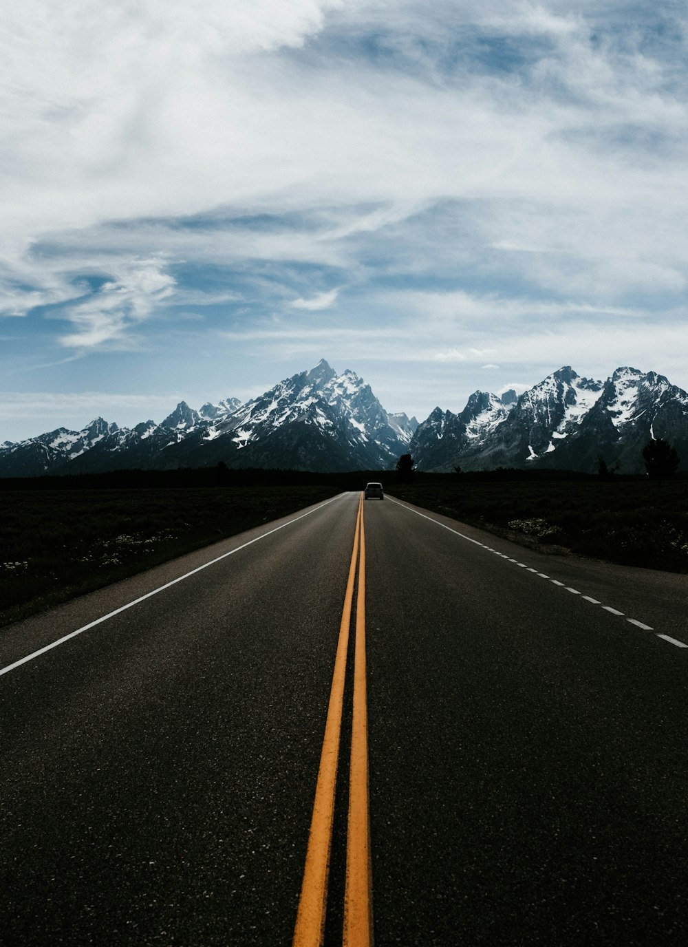 vehicle on straight countryside road leading to a mountain under blue skies