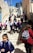 A group of children in school uniforms descends a stone staircase in an urban setting. The school uniforms consist of blue shirts and navy skirts, and many are carrying colorful backpacks. Adults accompany them, some wearing different attire. The scene is outdoors, with buildings lining the stairs and a clear blue sky above.