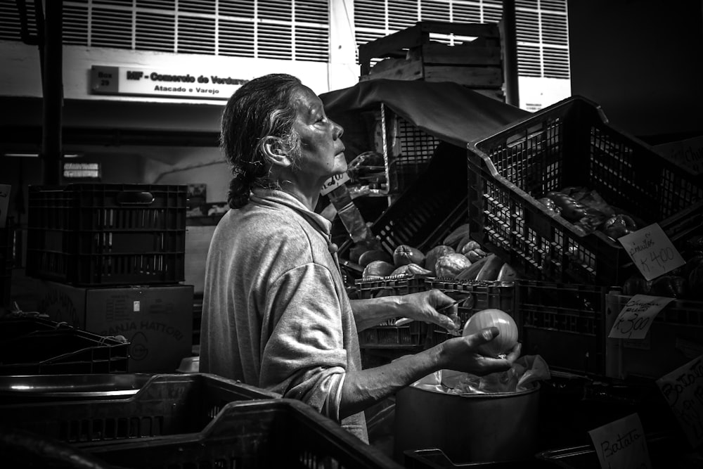 grayscale photography of woman holding round fruit near crates