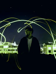 A mysterious figure silhouetted against a glowing gold-lit rooftop party.