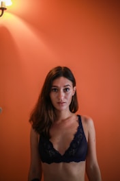 A woman smiling softly while wearing nude seamless shapewear, standing confidently in a bright, minimalist room.