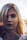 A close-up portrait of a person with long blonde hair, softly illuminated by the warm light of a setting sun, casting a gentle glow and creating lens flares. The background is out of focus, enhancing the central figure.
