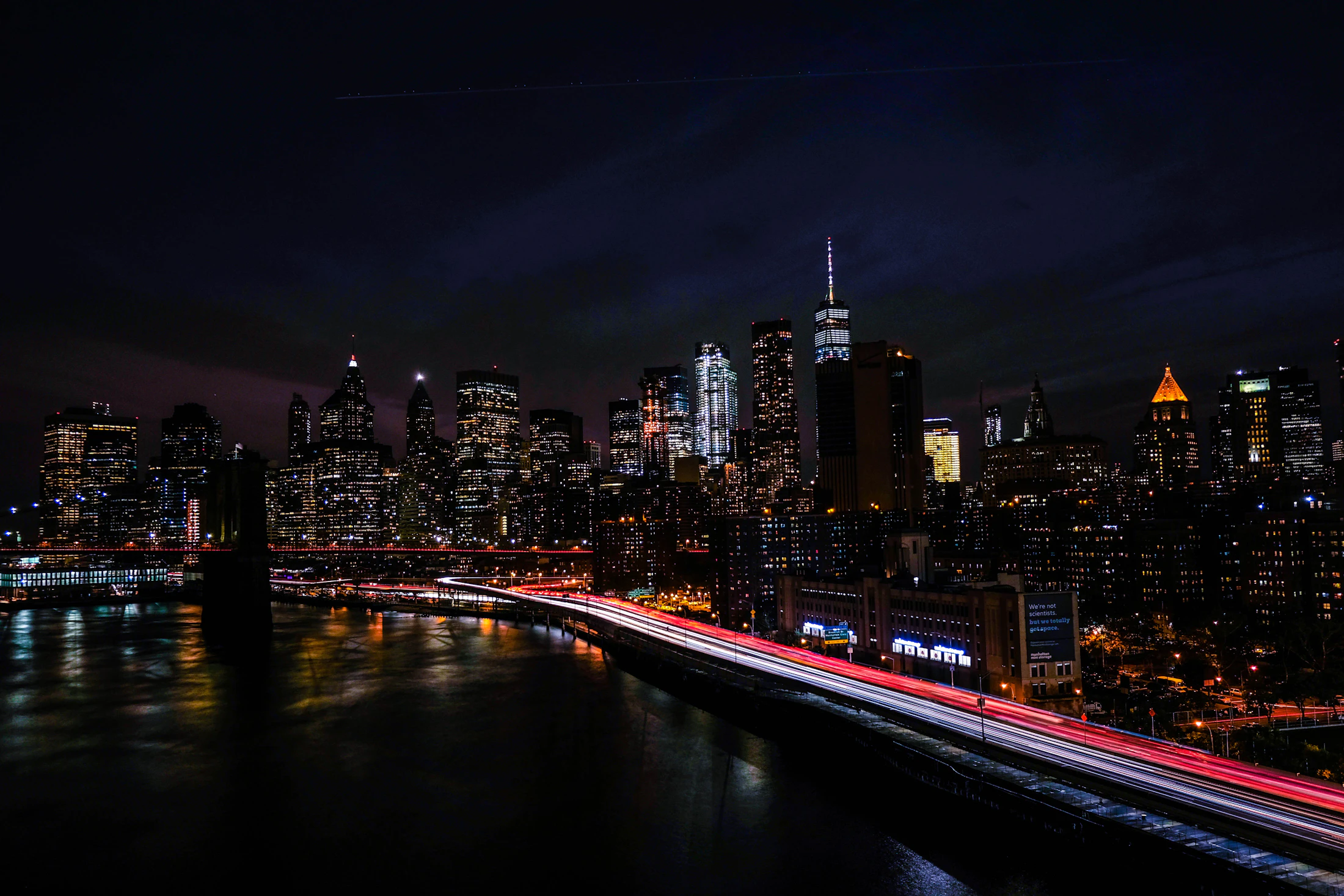 Manhattan skyline at night with the Brooklyn Bridge and red light trails