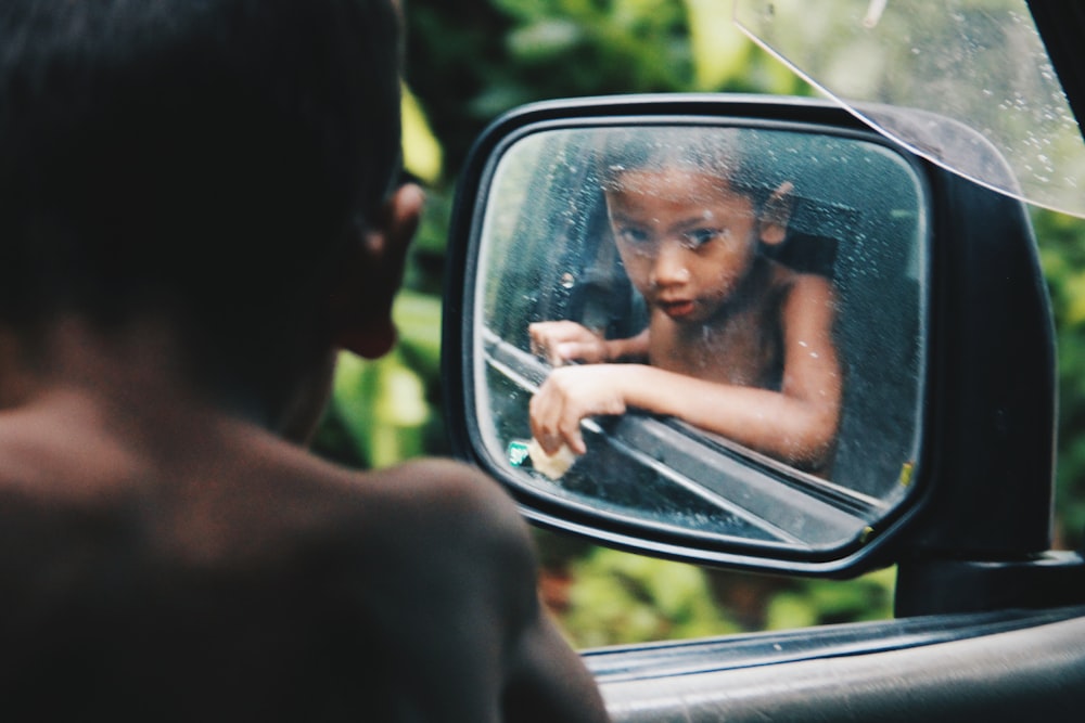 toddler looking at his reflection on wing mirror during daytime