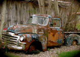 A classic 1940s pickup truck with faded paint parked beside a barn.