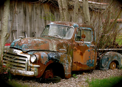 A classic 1940s pickup truck with faded paint parked beside a barn.